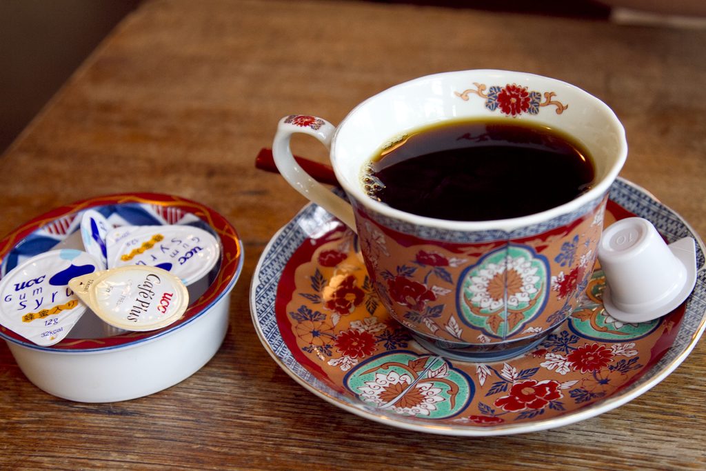 A patterned teacup on a saucer beside a small pot of cream